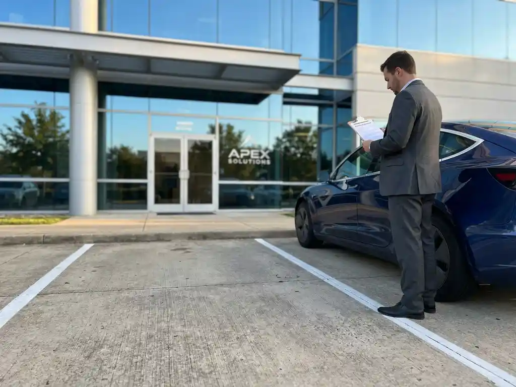Business professional in suit reviewing rental contract beside sedan in modern office building parking lot